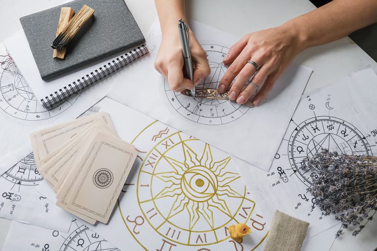 Mapa astral desenhado à mão, com cartas e um caderno sobre a mesa